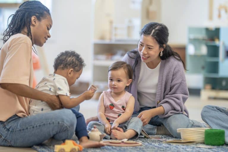 Mothers from diverse backgrounds interact with toddlers in a colorful and friendly setting, fostering education and play through social engagement and imaginative interactions.