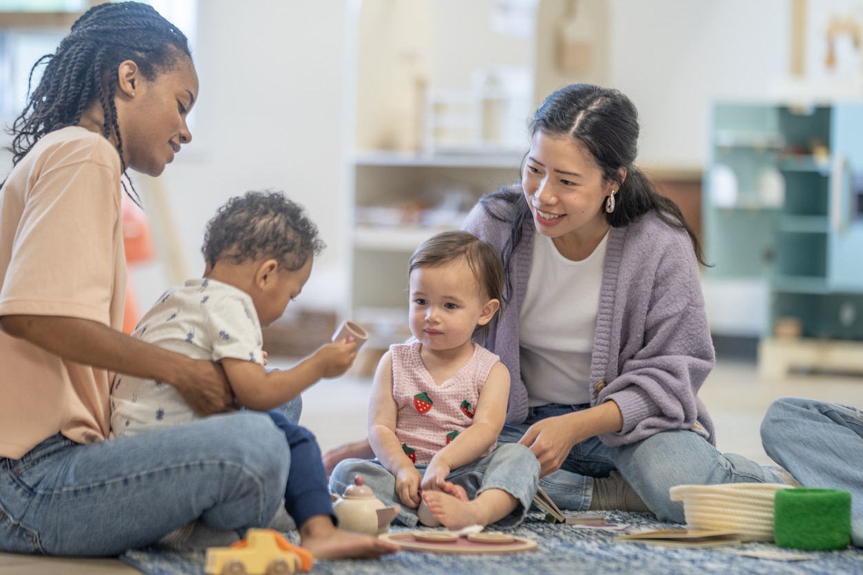 Mothers from diverse backgrounds interact with toddlers in a colorful and friendly setting, fostering education and play through social engagement and imaginative interactions.