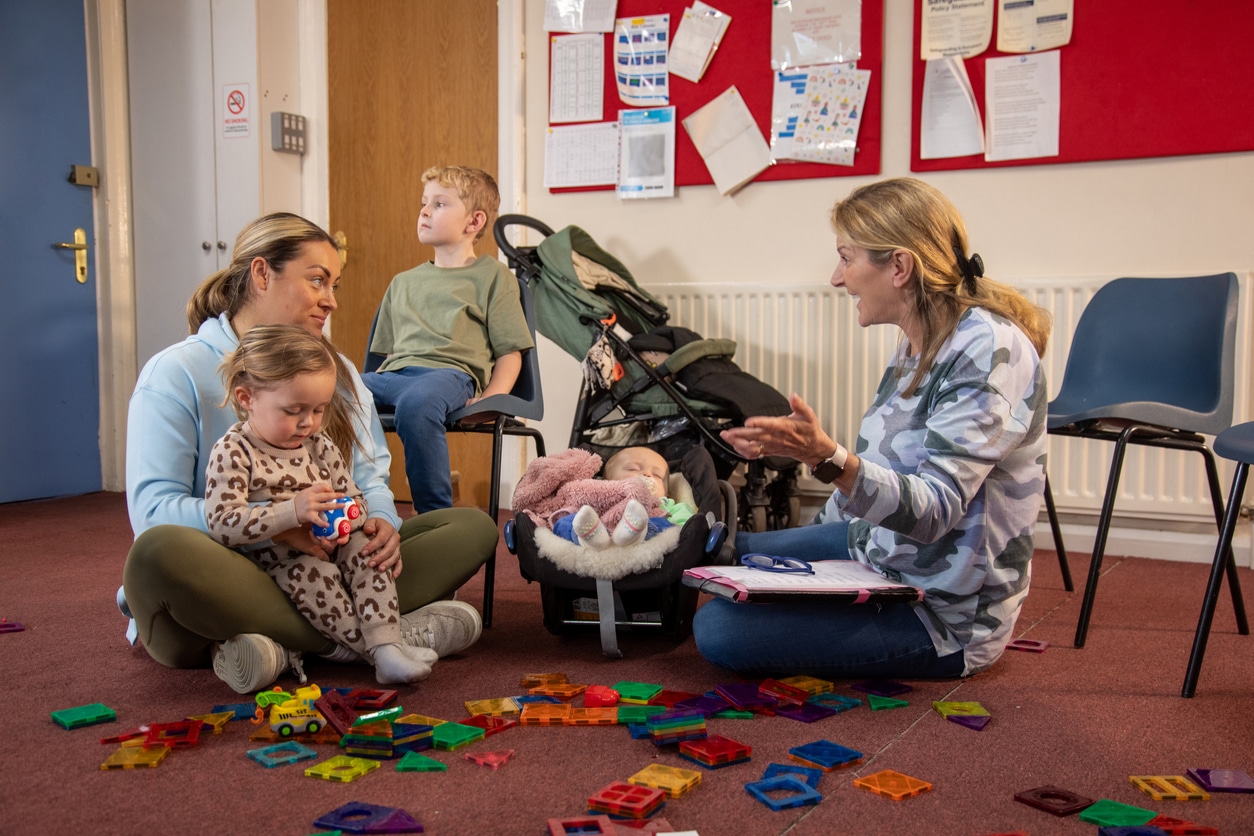 Full shot of a mother and her three children having a meeting with a childcare worker. They are in a community centre surrounded by toys.